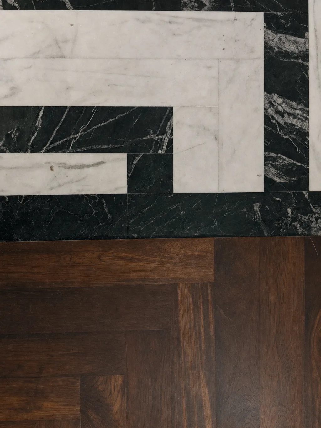 EPISODE Powai — Flooring material transition between concentric marble inlay and dark timber herringbone parquet.