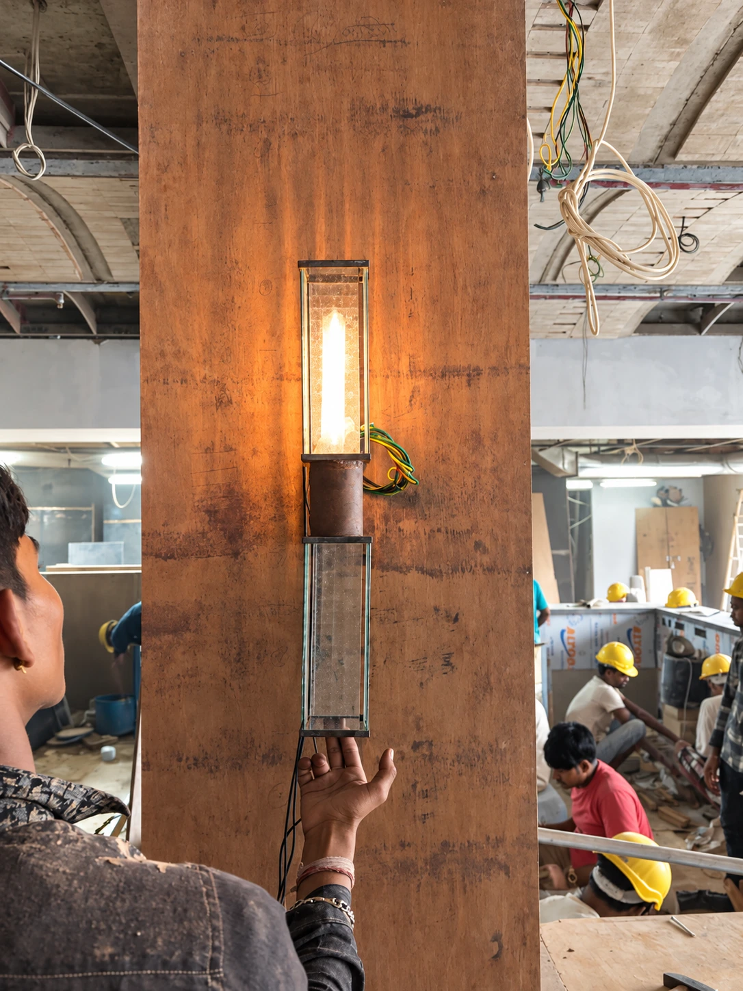 SOCIAL Vashi — Light prototype test. A lamp prototype is tested by hand during construction; exposed wiring and workers show the making stage.